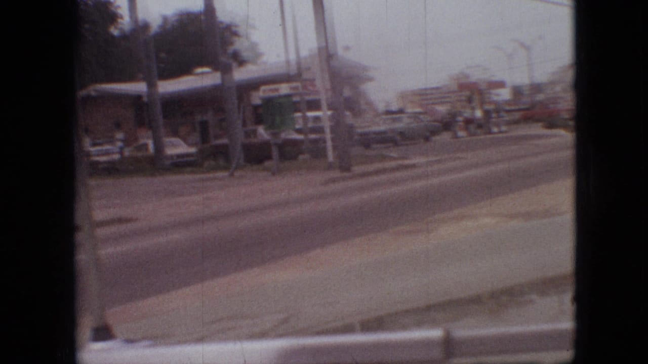 Gas station and roadside signs seen across the street from a moving vehicle.