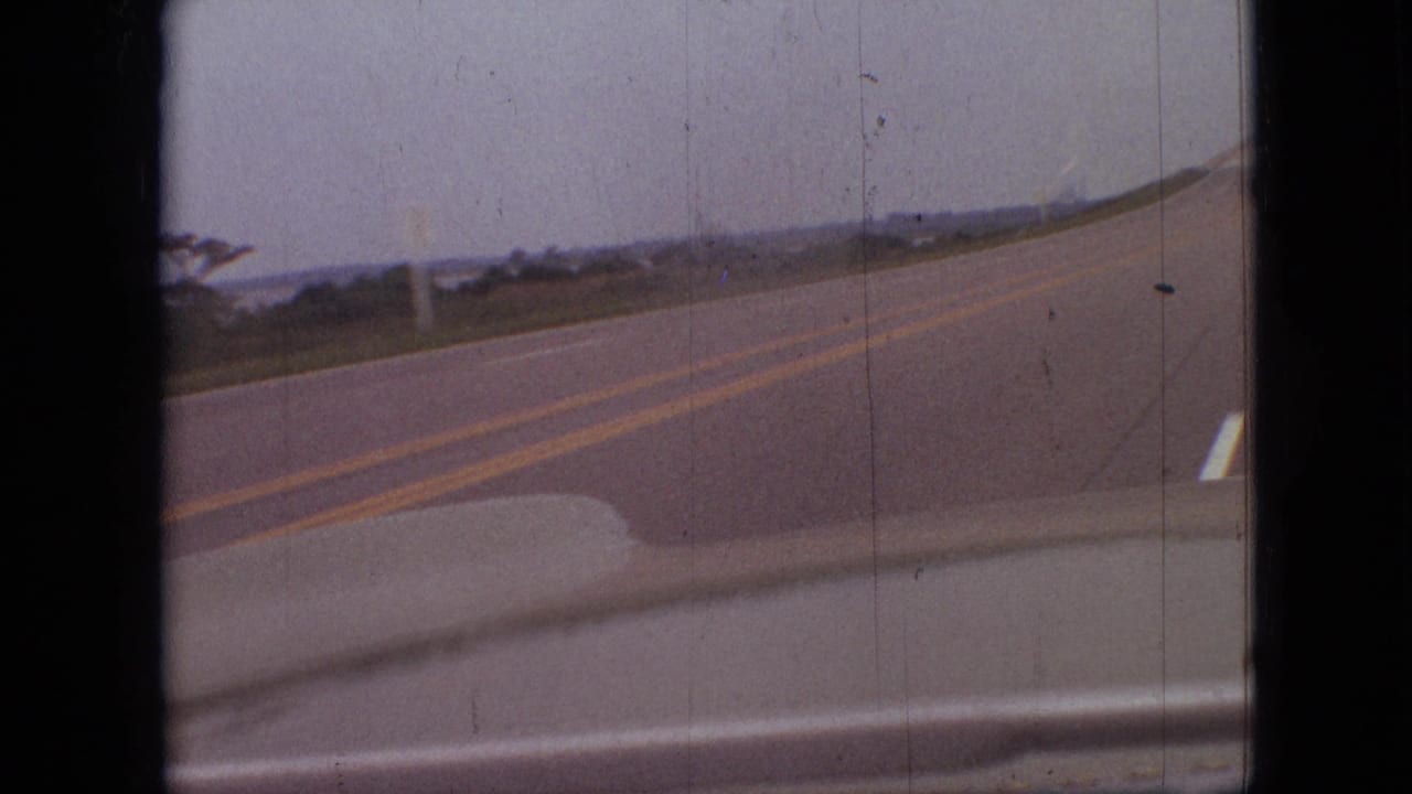 Two-lane highway bends through a low rural landscape with the car dashboard edge visible.