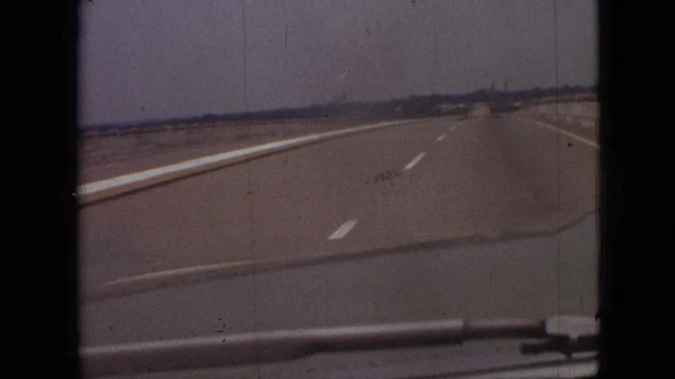 1968 8mm home-movie frame from near Branson, Missouri, showing a forward car view along a wide flat highway with lane markings and a low distant horizon.