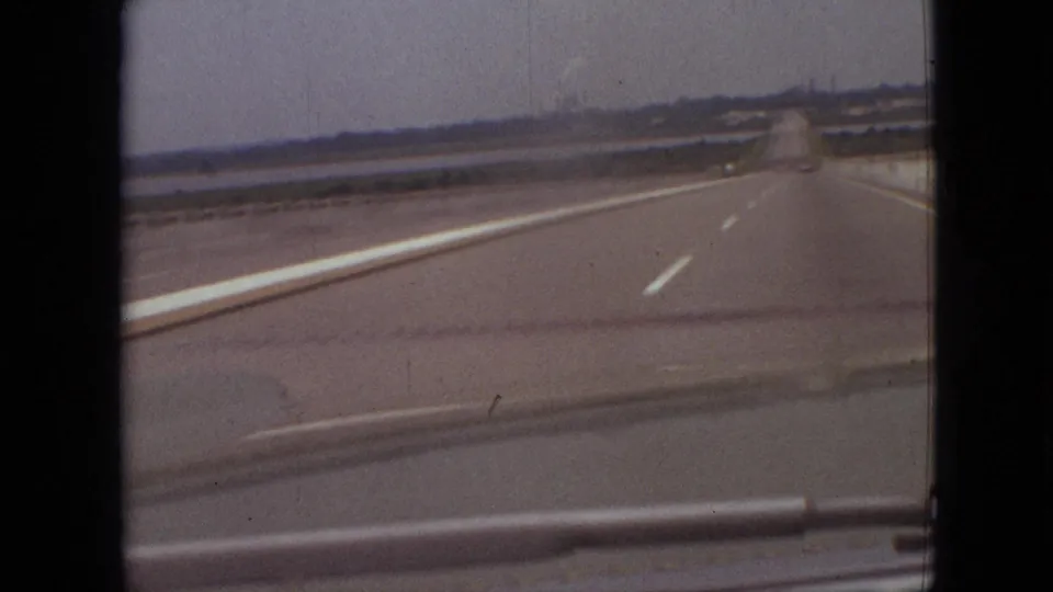 Final 1968 8mm frame of the Branson, Missouri highway view, with the road narrowing toward the horizon, a faint smoke plume, distant vehicles, and visible film-frame borders.