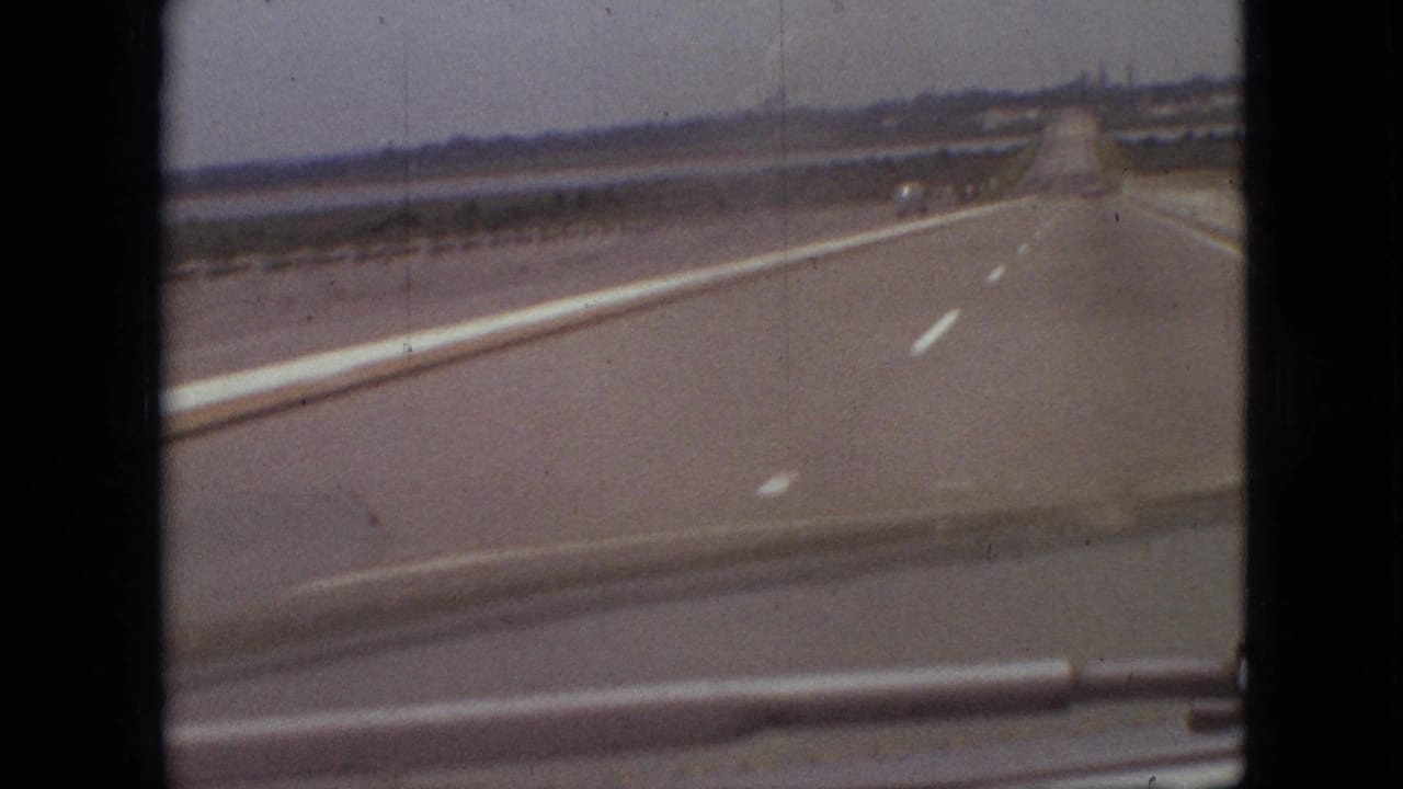 Wide paved road seen through a vehicle windshield with sparse traffic far ahead.