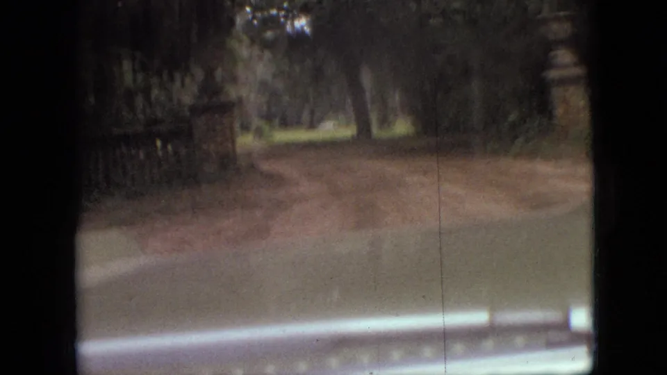 1968 Branson, Missouri 8mm frame showing a soft, shaky windshield view down a wooded dirt road, with the vehicle hood and roadside foliage visible.