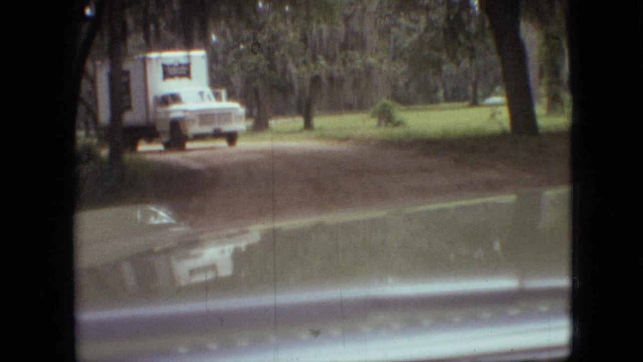 1968 Branson, Missouri home-movie frame showing a white delivery truck ahead on a dirt road, viewed from inside a car with windshield edges visible.