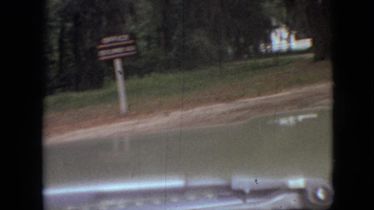 A roadside signpost appears beside a wooded road in Branson, Missouri, filmed from a moving vehicle in 1968 home-movie footage.