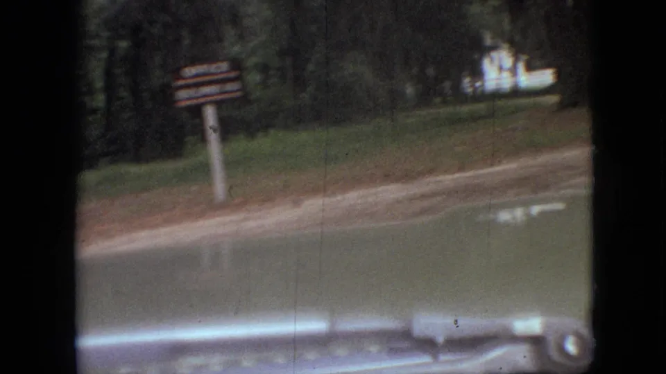 A roadside signpost appears beside a wooded road in Branson, Missouri, filmed from a moving vehicle in 1968 home-movie footage.