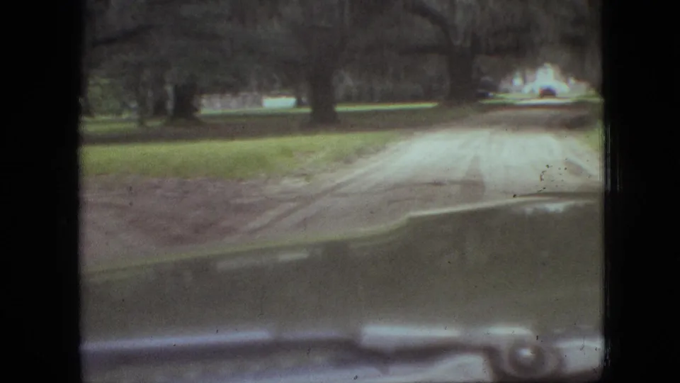 Windshield view down a pale dirt road through wooded grounds toward a distant white house or building in Branson, Missouri, 1968.