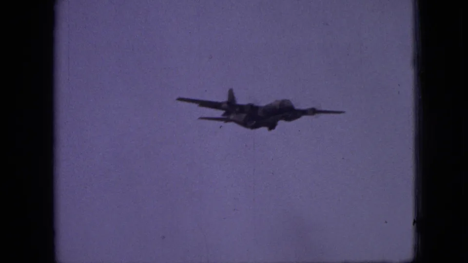 A propeller aircraft appears in silhouette against a pale purple sky in 1968 8mm home-movie footage from Branson, Missouri.