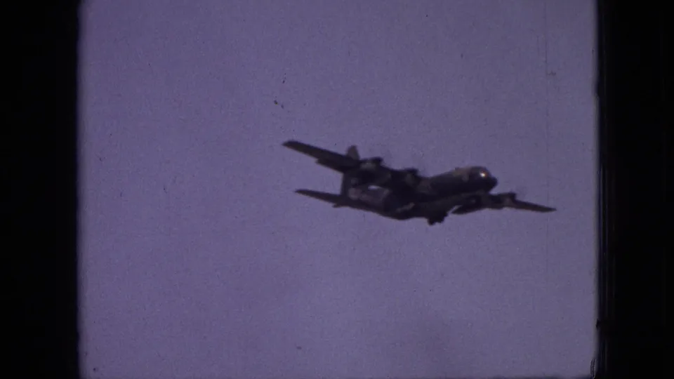 A twin-engine propeller plane flies across a muted sky, framed by dark 8mm film edges in the Branson, Missouri home-movie clip.