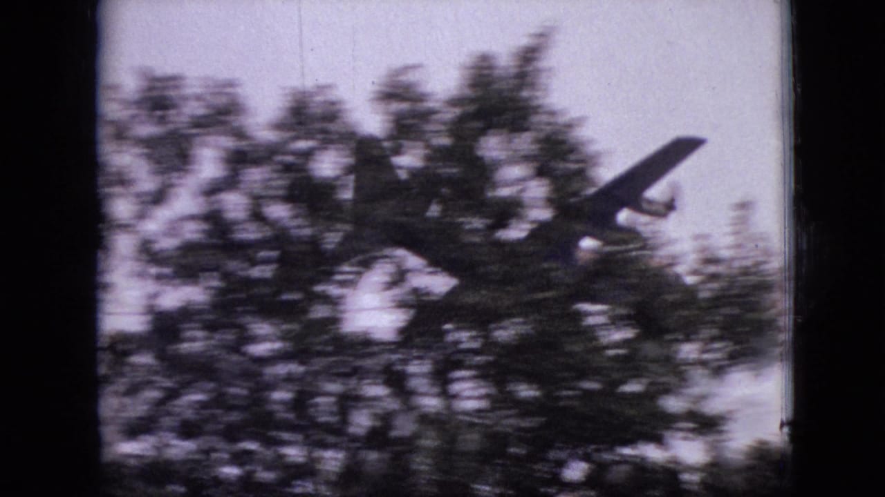 A small propeller airplane emerges above the treeline in metadata-supported 1968 Branson, Missouri home-movie footage, framed by soft grain and dark scan edges.