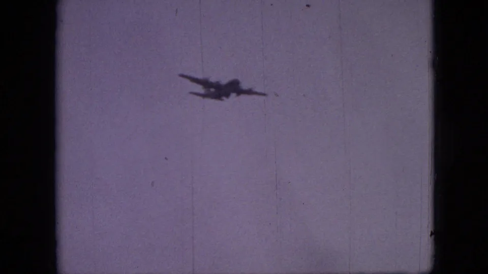 The aircraft is seen at a distance against a plain gray sky in 1968 Branson, Missouri 8mm footage, with muted color and visible film texture.