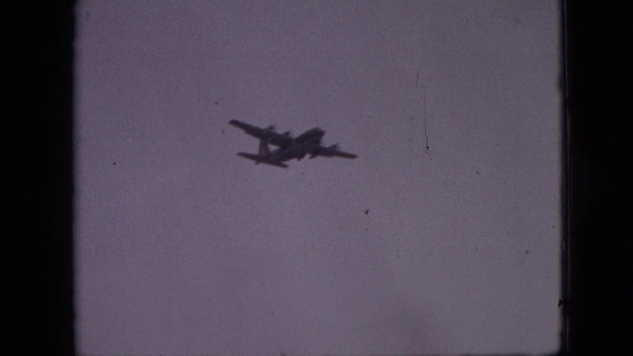 Distant four-engine aircraft appears as a dark silhouette against a pale sky in 1968 Branson, Missouri home-movie footage.