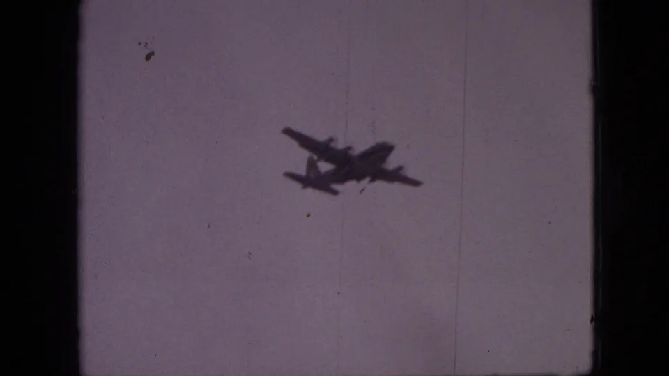 A small four-engine aircraft silhouette moves across the pale sky in a 1968 Branson, Missouri 8mm home-movie frame.