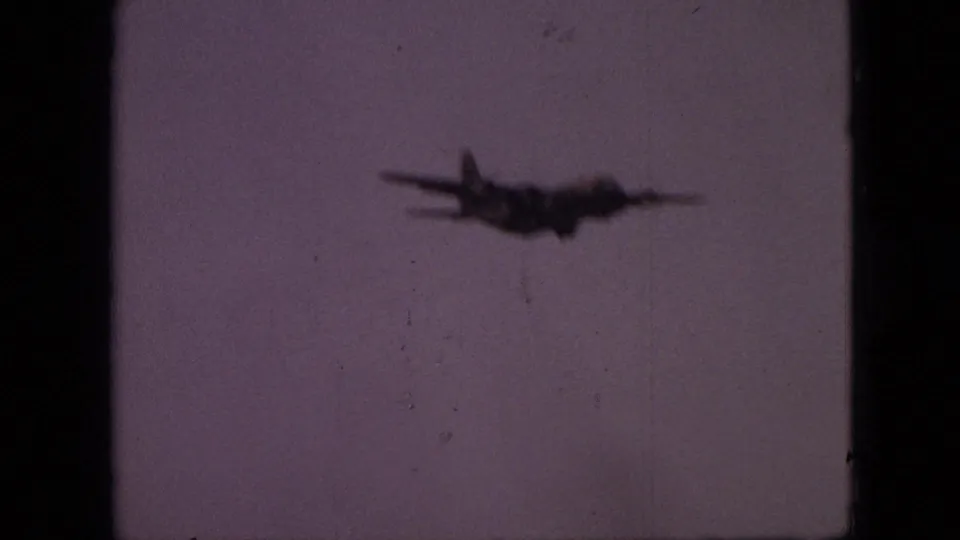 A blurred four-engine aircraft silhouette is centered lower in the frame against a faded purple-gray sky in 1968 Branson, Missouri home-movie footage.