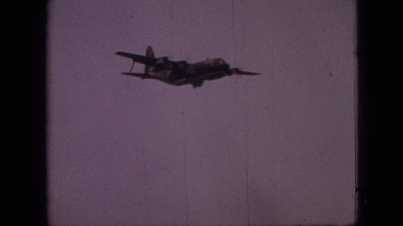 A military-style transport aircraft flies across a pale purple sky in 1968 Branson, Missouri home-movie footage.