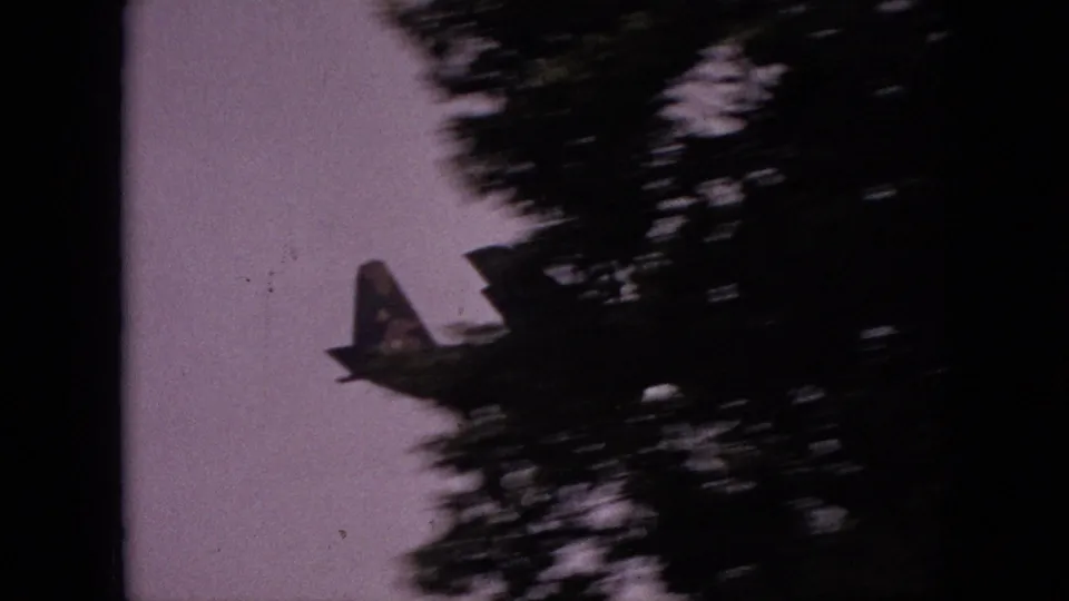 The aircraft passes near dark treetops in grainy 1968 Branson home-movie footage, with heavy blur and film borders visible.