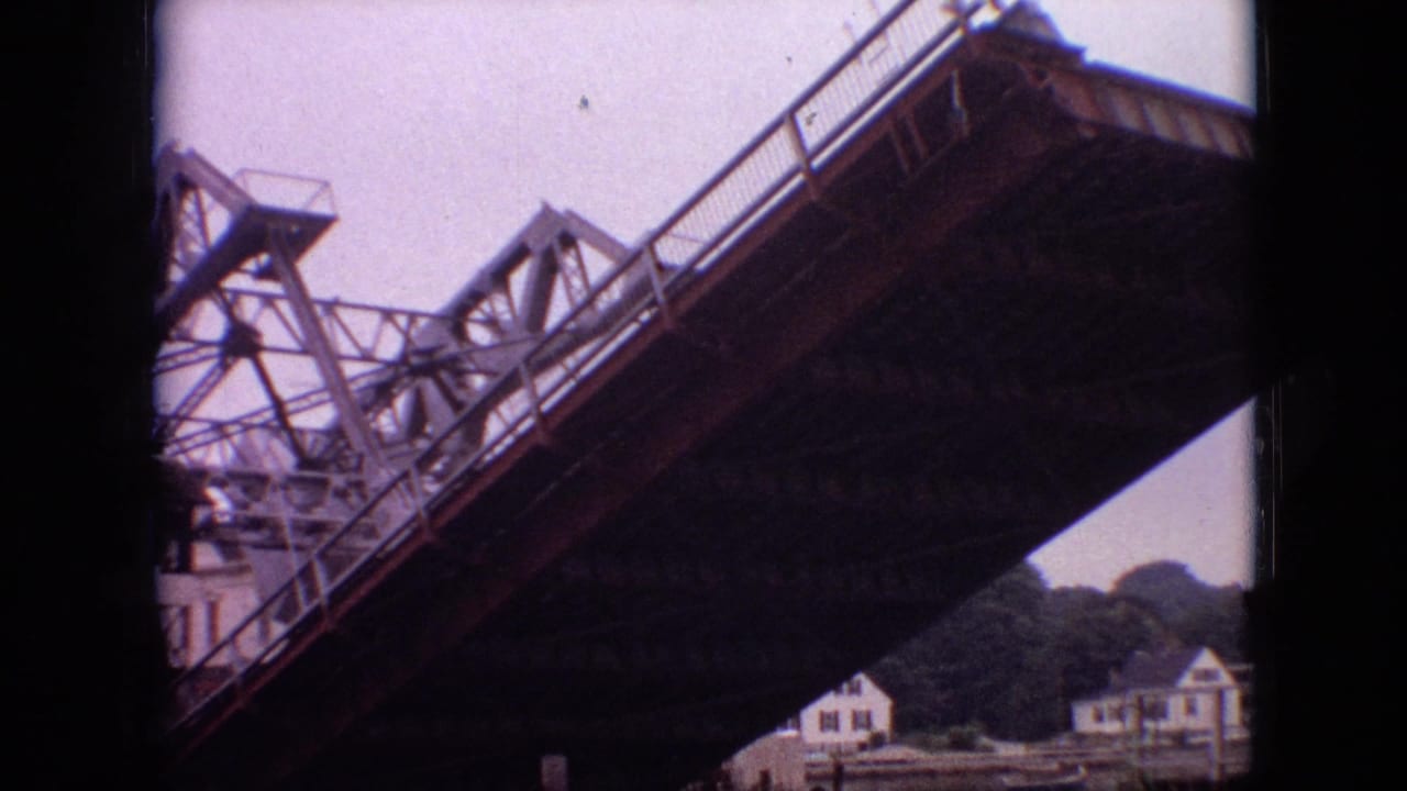 1968 Branson, Missouri 8mm frame showing a steel drawbridge lifting above a river area, with small houses and trees visible in the background.