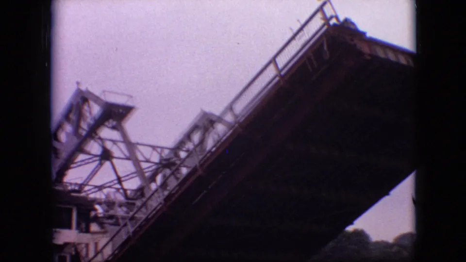 1968 home-movie frame from Branson showing the drawbridge structure from below, with trusswork, railings, and blurred mechanical detail visible.