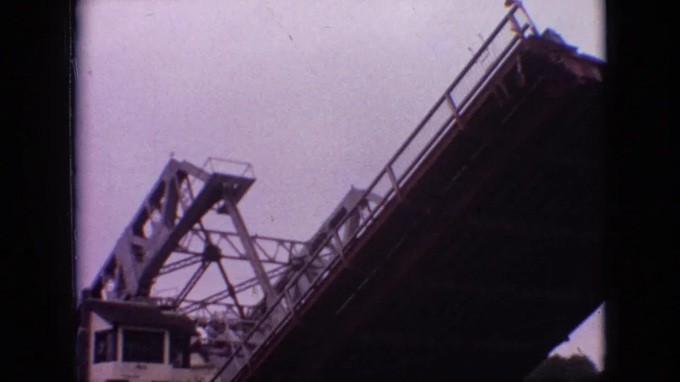 Low-angle Branson drawbridge frame showing the raised span, steel support structure, railing, and part of a small riverside building beneath it.