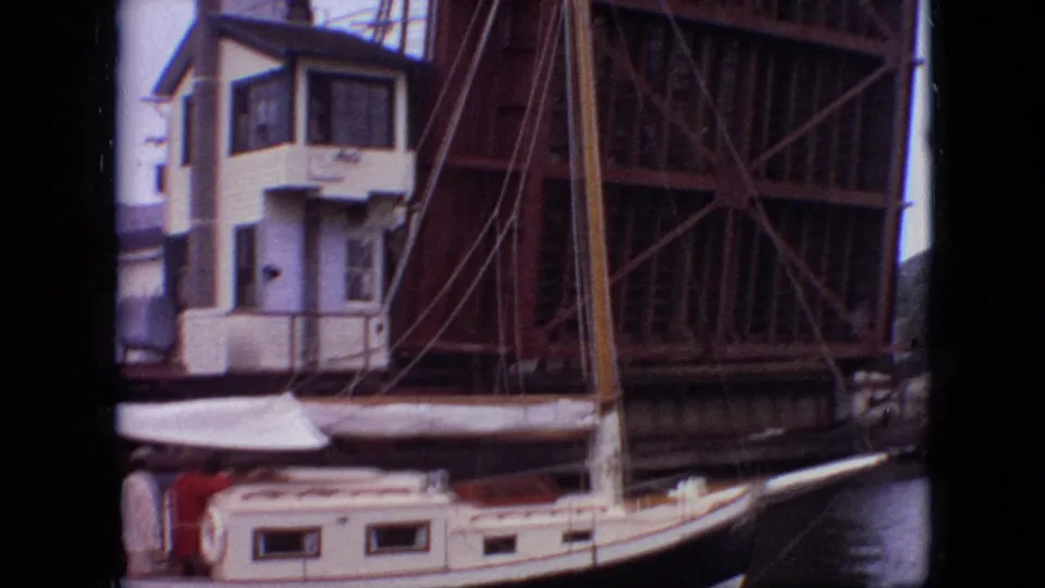1968 Branson, Missouri 8mm frame showing the sailboat below a raised steel drawbridge, with a white bridge-control structure and mast visible above the cabin.