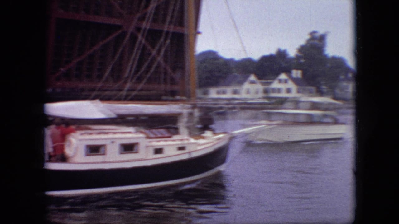 White-and-black sailboat passing beneath an opened drawbridge near riverside houses.