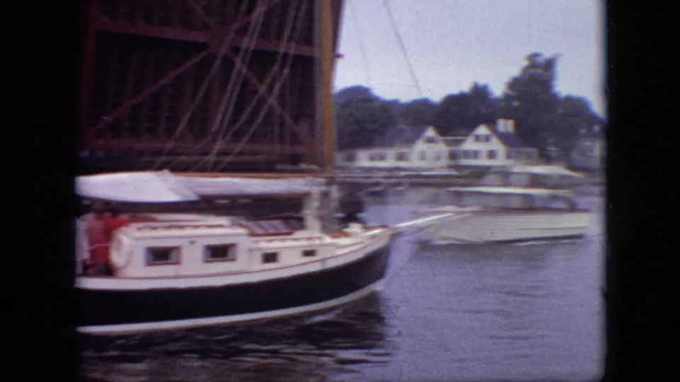 A white-and-black sailboat moves under the raised drawbridge in Branson, Missouri, with riverside houses visible beyond the water.