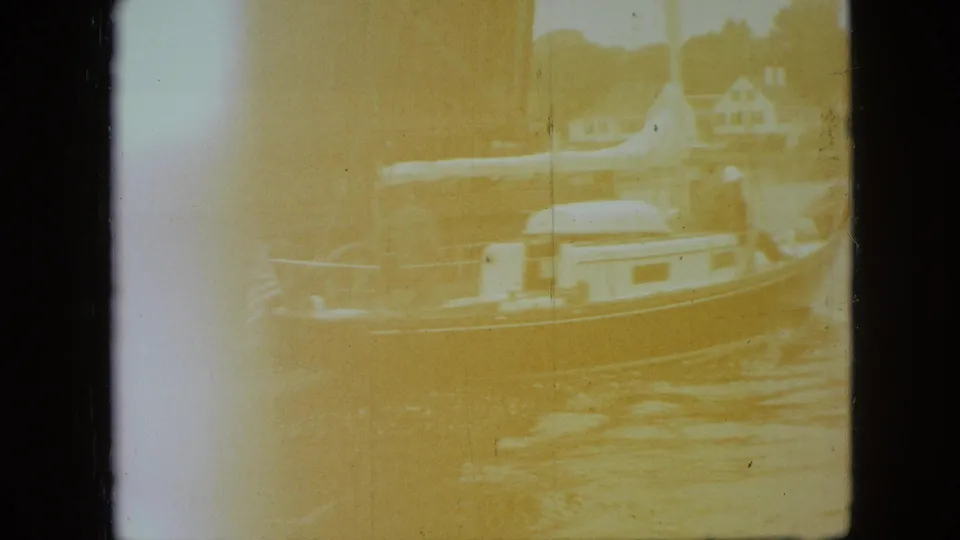 Faded 8mm frame from the Branson river scene, with the sailboat, water, and distant houses still faintly visible through a yellow exposure shift.