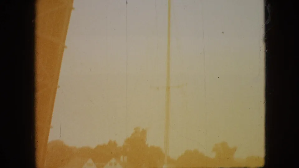 Washed 8mm frame from the end of the Branson river clip, showing a faint mast or rigging line, bridge edge, treetops, and shoreline houses through heavy exposure shift.