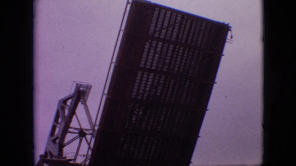 1968 Branson, Missouri home-movie frame with a raised metal bridge span and mechanical support structure dominating the view.