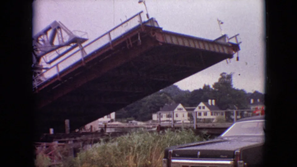 A handheld 8mm frame from Branson, Missouri in 1968 shows the drawbridge continuing downward, with the bridge underside dominating the view and a late-1960s car at the lower right.