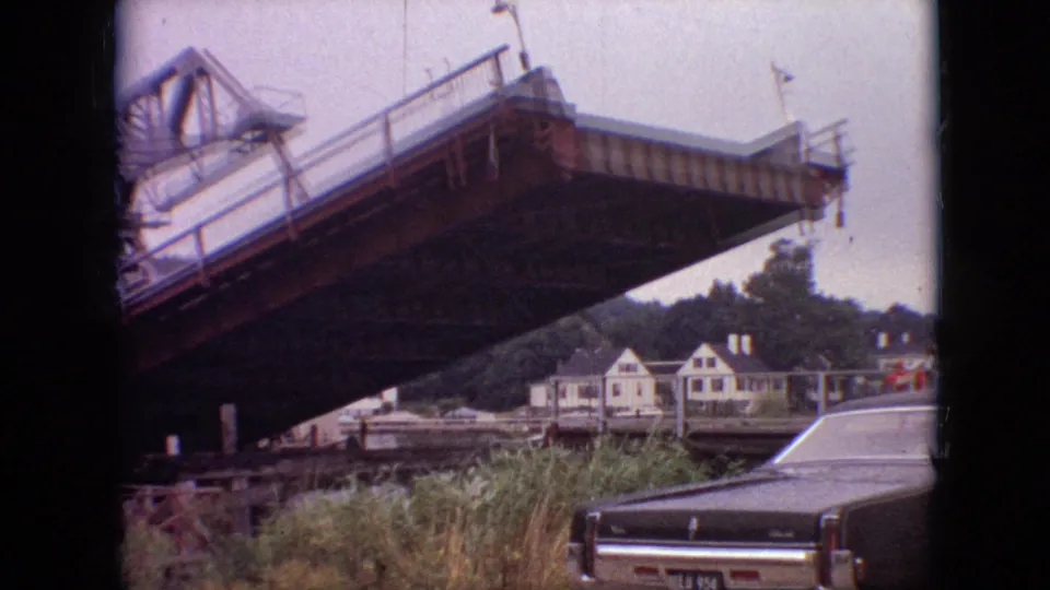 By the final 1968 Branson, Missouri frame, the drawbridge span is closer to level, with white houses, green trees, tall grass, and a parked car visible below.