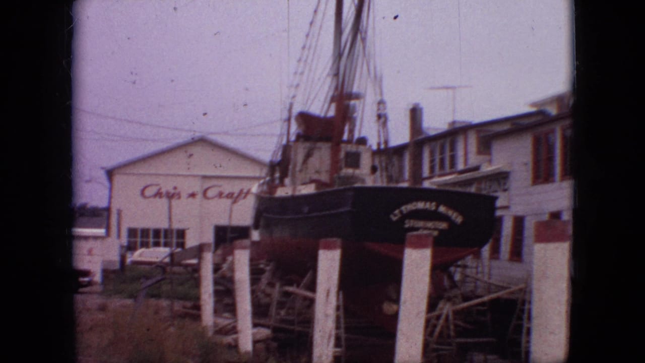 1968 Branson, Missouri 8mm frame showing a black fishing vessel on blocks beside white posts, with rigging above and a signed boatyard building behind it.