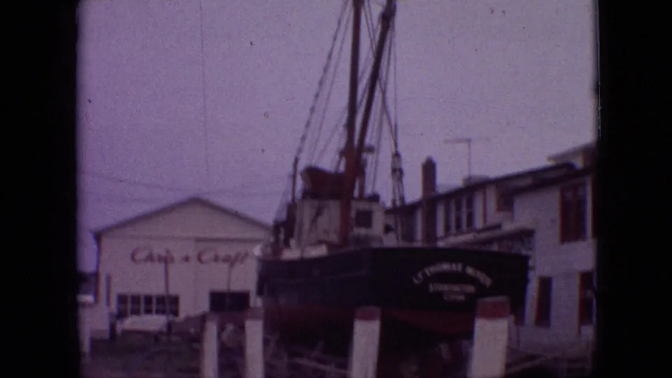 1968 Branson, Missouri home-movie frame showing the vessel from a slightly shifted angle, with soft focus, support posts, rigging, and the signed building in the background.
