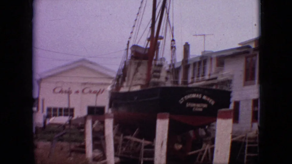 1968 Branson, Missouri 8mm frame showing the black vessel resting on supports, with white posts in front, rigging above, and Chris-Craft-related signage visible on the building behind.