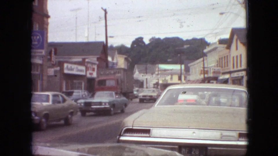 1968 Branson, Missouri street view with classic American cars, storefront signs, utility poles, and a dashboard-level home-movie perspective.