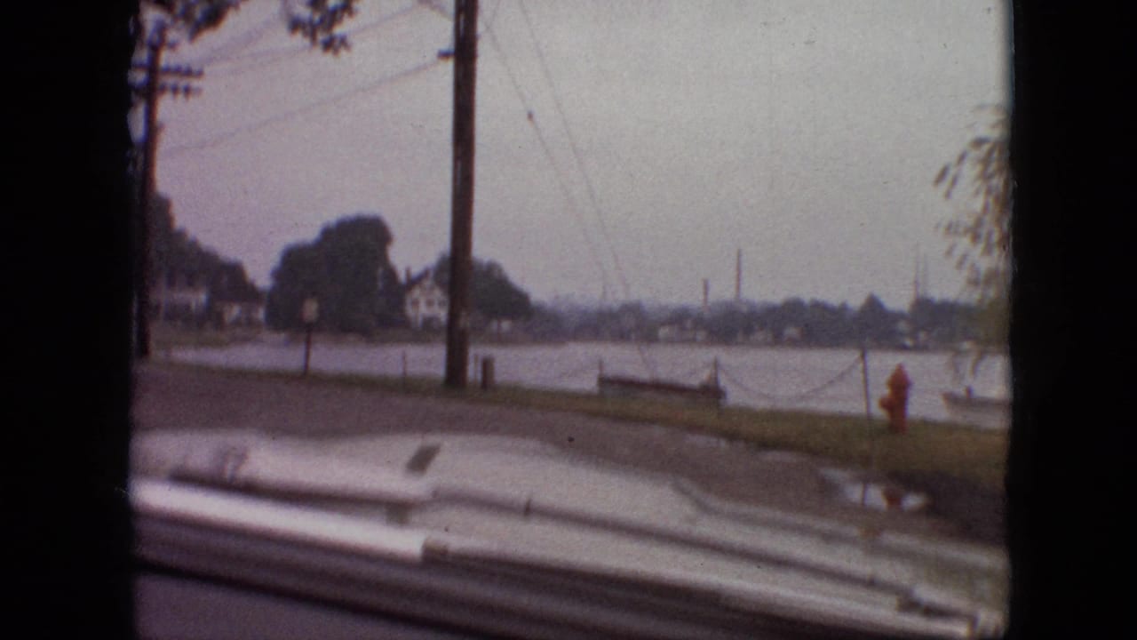 1968 Branson, Missouri 8mm frame from a moving car showing a lakeside residential road, utility poles, houses, a red fire hydrant, and the car hood at the bottom edge.