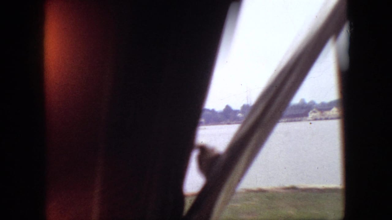 Lake seen through a vehicle window with shoreline and window frame in the foreground.