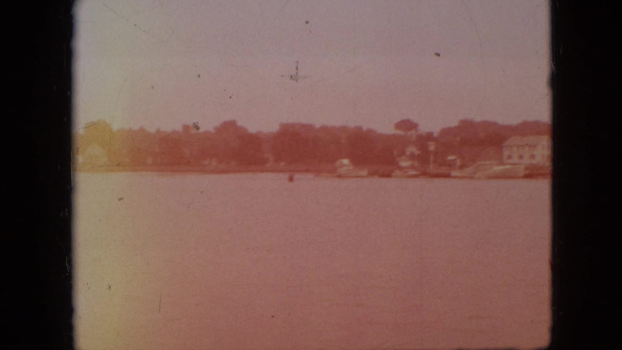1968 Branson, Missouri 8mm frame showing a hazy view across lake water toward low shoreline buildings and trees.