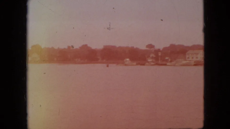 1968 Branson, Missouri 8mm frame showing a hazy view across lake water toward low shoreline buildings and trees.