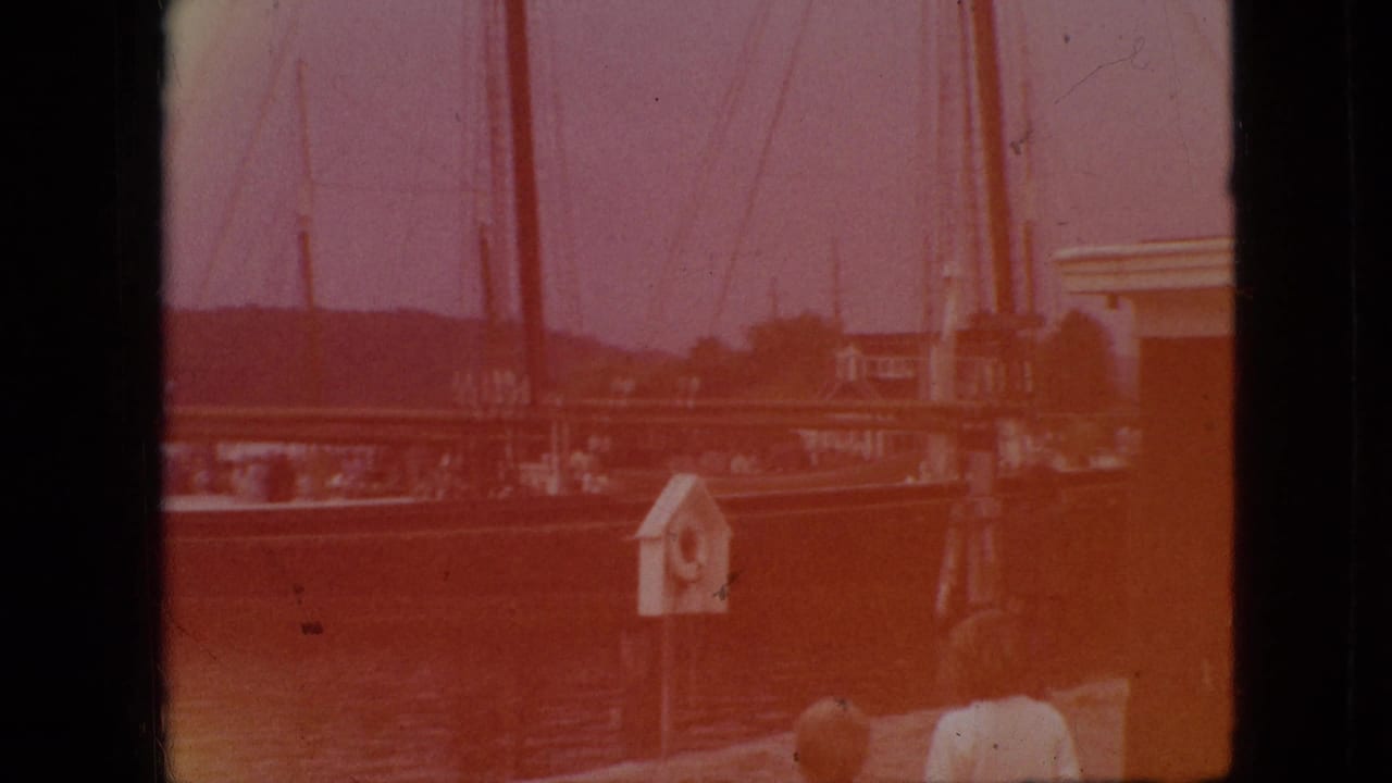 Docked sailboat with tall masts near a lakeside structure and partial figures.