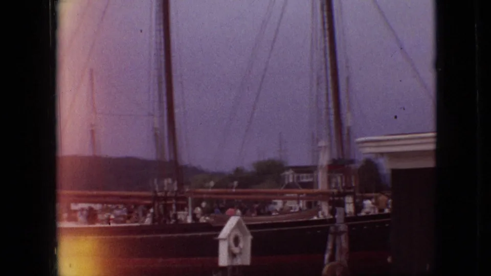 1968 Branson, Missouri 8mm frame looking across a docked sailboat with visible rigging, shoreline buildings, and a small white dockside structure in the foreground.