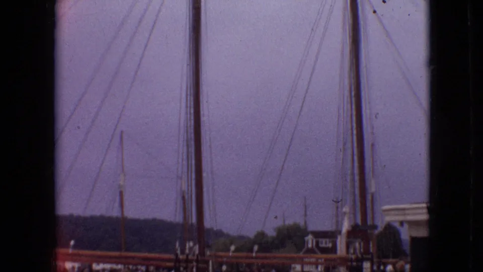 1968 Branson, Missouri frame emphasizing tall sailboat masts and rigging above the dock, with shoreline and a partial building visible beyond.