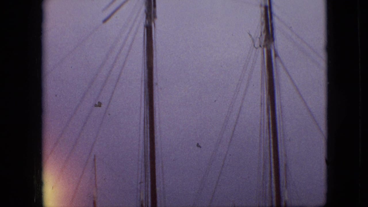 1968 Branson, Missouri home-movie frame showing sailboat masts and rigging seen through dark vertical frame edges against a purple-blue sky.