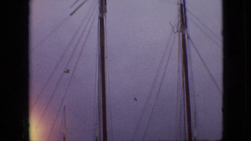 1968 Branson, Missouri home-movie frame showing sailboat masts and rigging seen through dark vertical frame edges against a purple-blue sky.