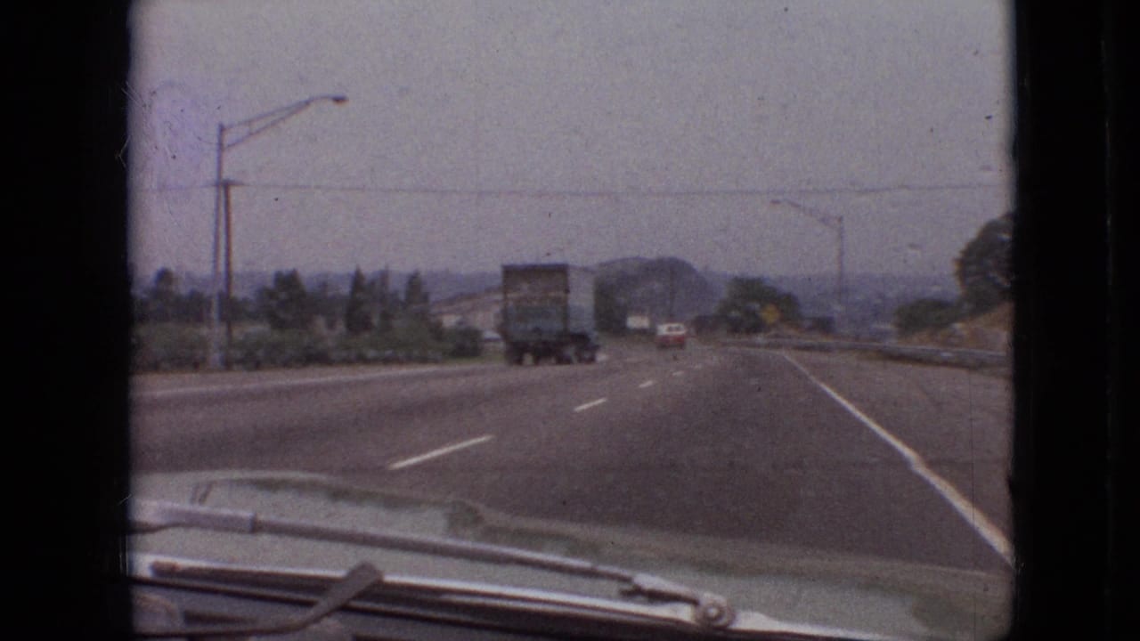 Car follows a semi-truck on a curving highway under an overcast sky.