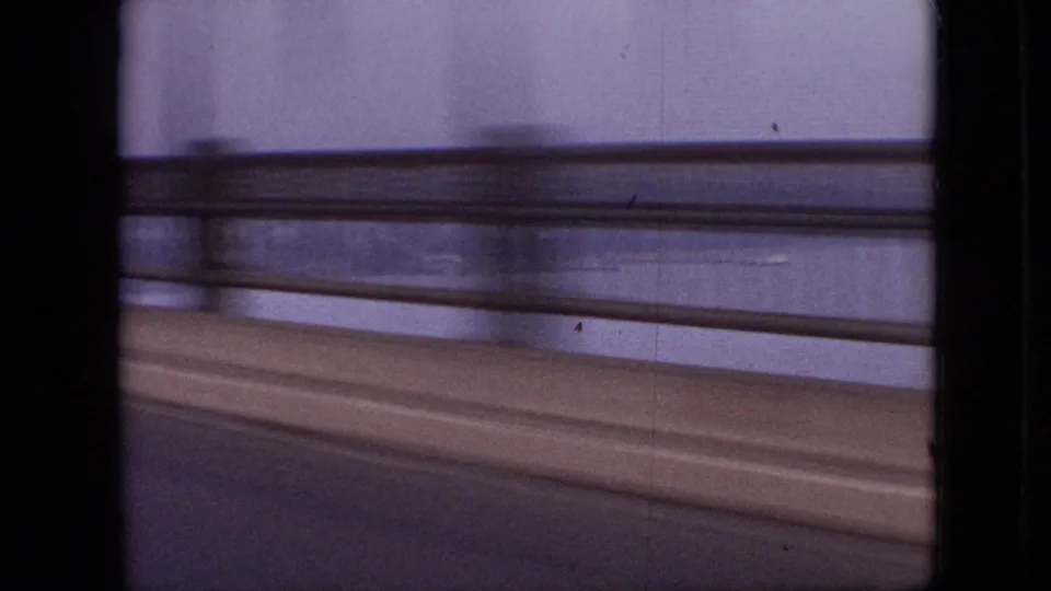 Moving-car view across a bridge in the stated Branson, Missouri clip, with concrete railing, water beyond the span, and strong motion blur from the 8mm camera.
