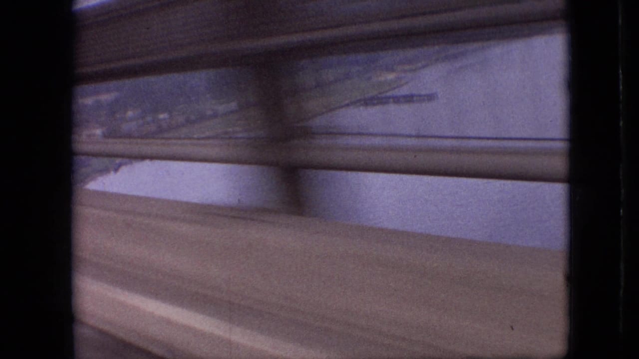 View through dark vertical and horizontal frame edges toward water, shoreline, and a blurred road or guardrail.