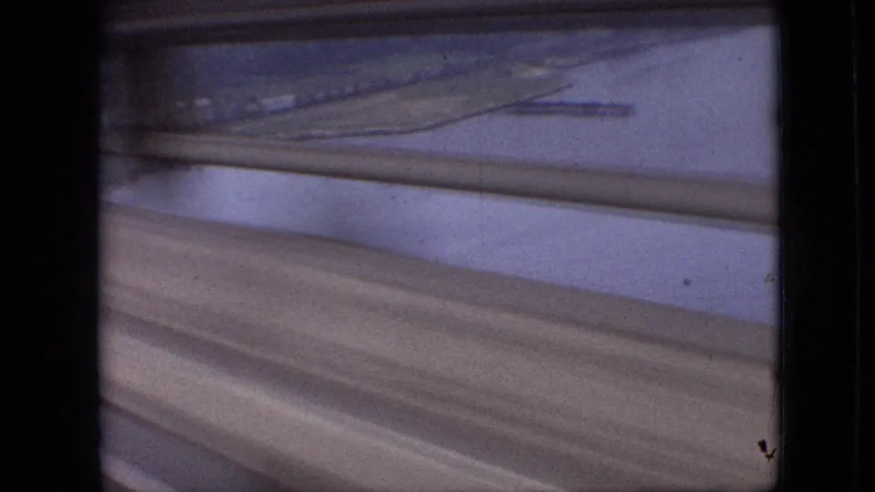 1968 Branson, Missouri frame looking past window slats toward water, land, and diagonal roadway or guardrail bands with faded 8mm color.