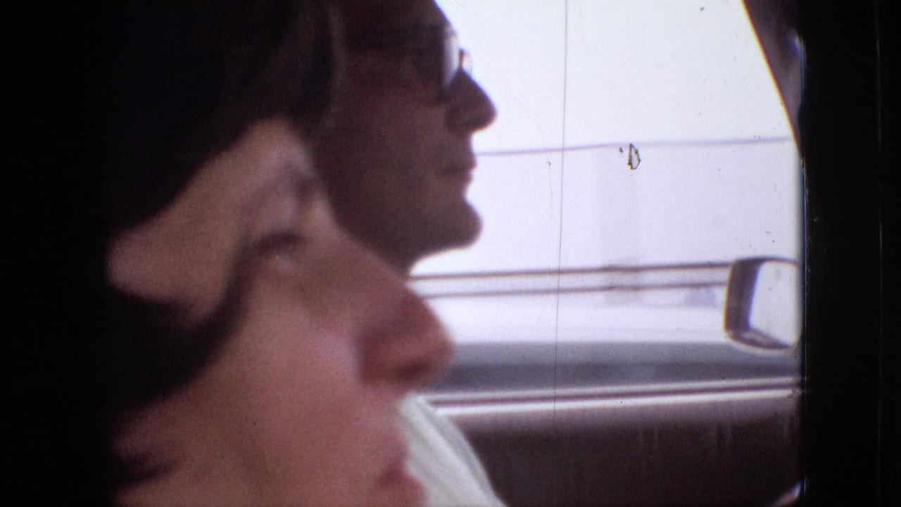 Inside a moving car in the supplied 1968 Branson, Missouri clip, a dark-haired passenger is seen in soft profile while a driver wearing glasses appears beyond her.
