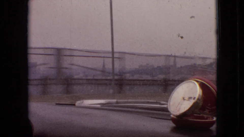 1968 Branson, Missouri home-movie frame from inside a car, showing the dashboard, windshield wipers, roadside railings, and a small red-and-white dashboard object through soft focus.