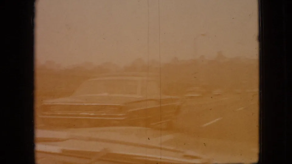 Sepia-toned 1968 road-travel frame from Branson, Missouri footage, with a pale classic automobile passing through a hazy, color-shifted highway view.